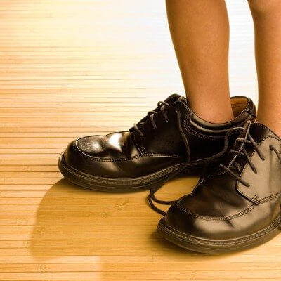 Life Skills: Big shoes to fill child's feet in large grown-up black shoes on backlit wood floor playing dress-up